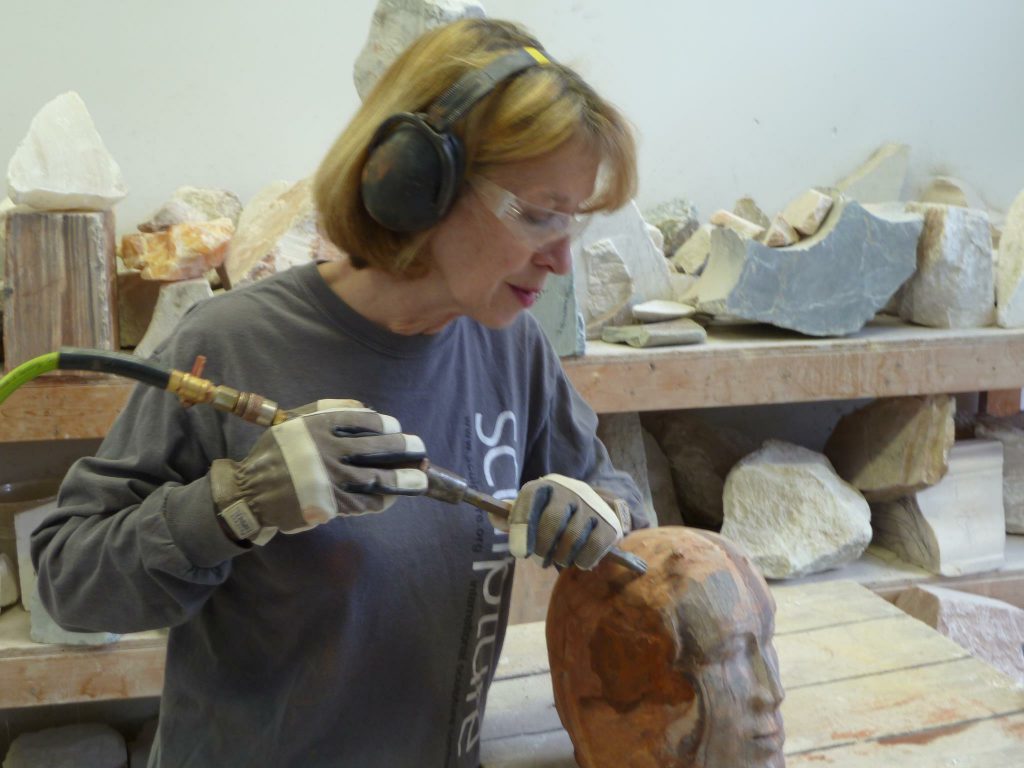 A woman wearing ear muffs and gloves working on a piece of art.